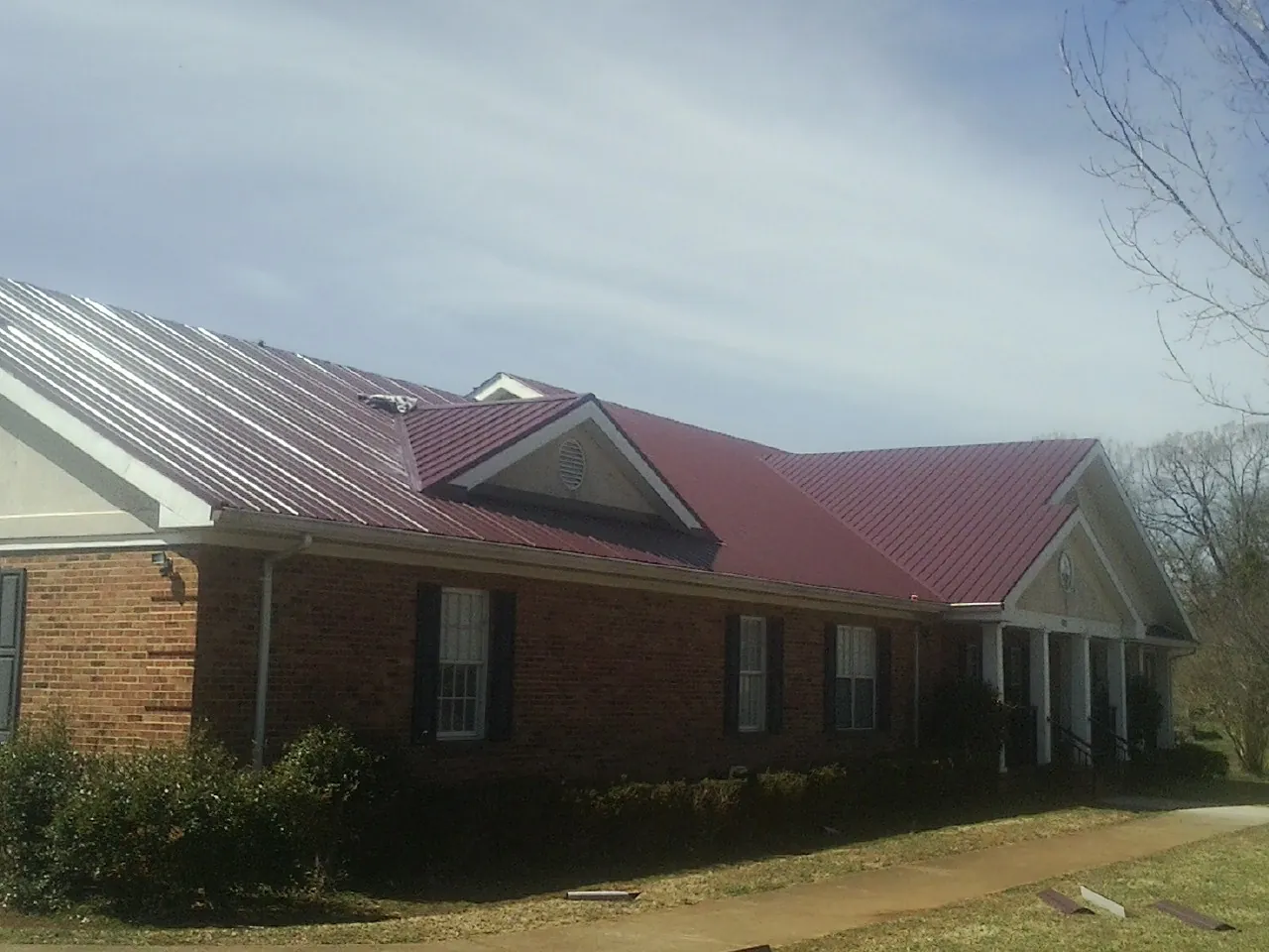 Red metal roof with gabled entries on a long brick building, from a Hail Damage Roof Repair job in Sayville