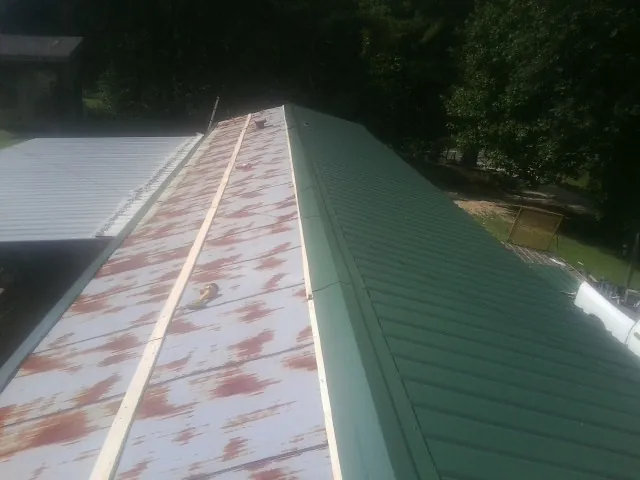 Old rusted panels beside newly installed green metal roofing — Wind Damage Roof Repair by Roofing Brothers in Sayville