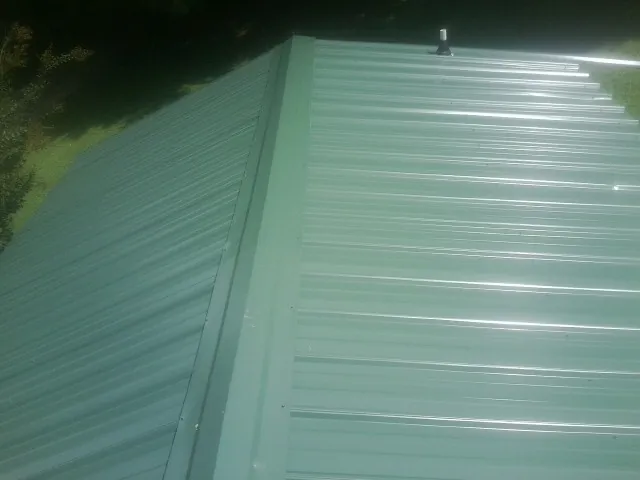 New green metal panels meeting at the ridge of a roof — Flat Roof Repair work by our crew in Sayville