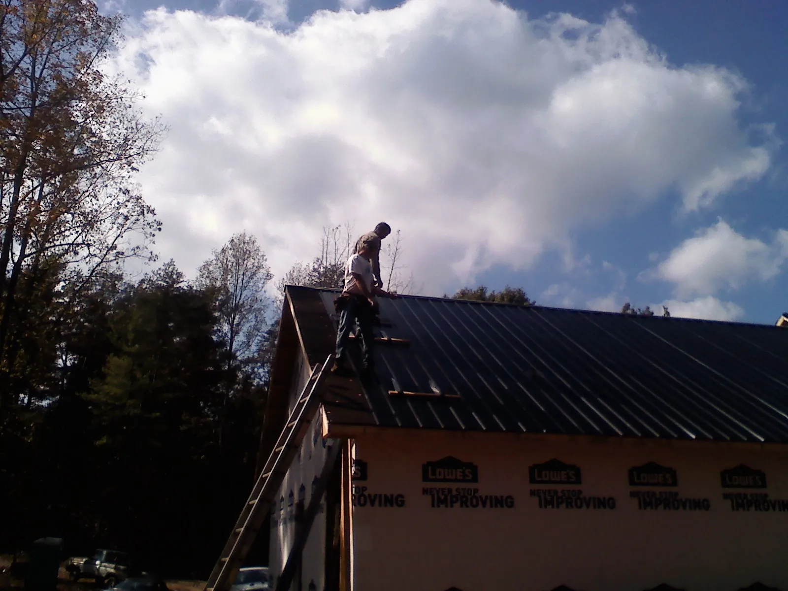 Roofer fastening dark metal panels high against a cloudy sky, from a Roof Inspection job in Sayville