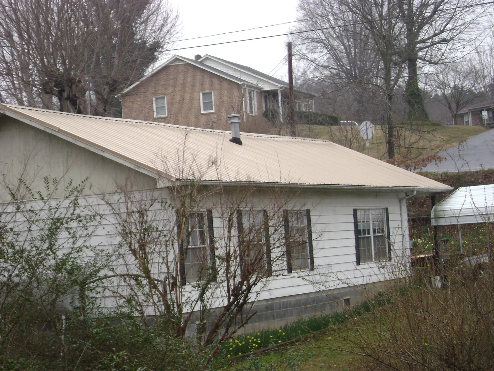 Tan metal roof on a white sided house set into a hillside — Commercial Roofing by Roofing Brothers in Sayville