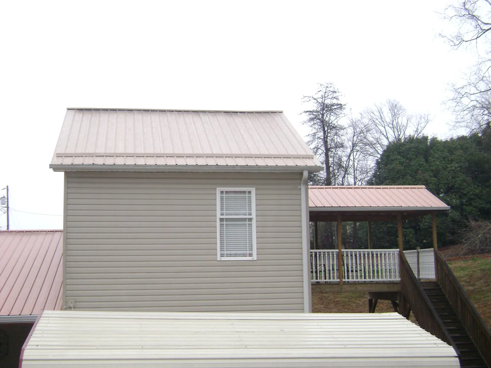 Tan metal roofs on a two story addition and attached porch, from a Roof Replacement job in Sayville